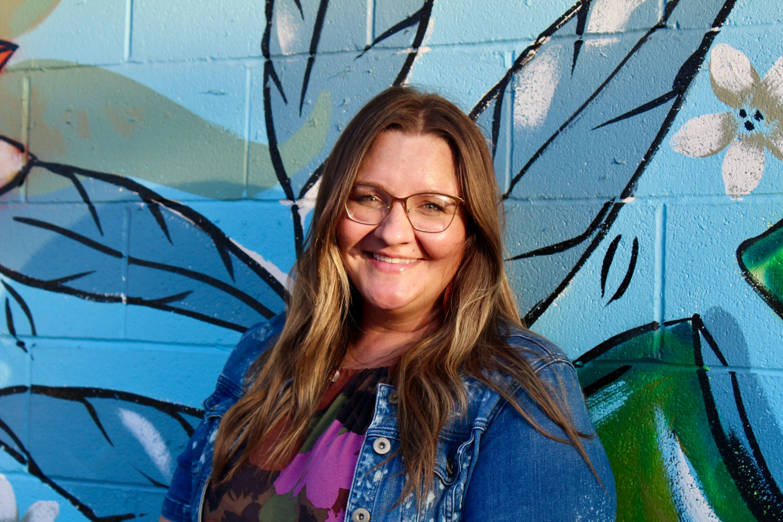 Headshot-style mural of a smiling woman, painted in vibrant tones with a colorful backdrop.